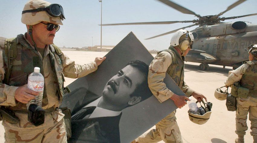 جنود أميركيون في مطار بغداد مع صورة لصدام حسين بعد إطاحة نظامه يوم 14 أبريل 2003 - AFP