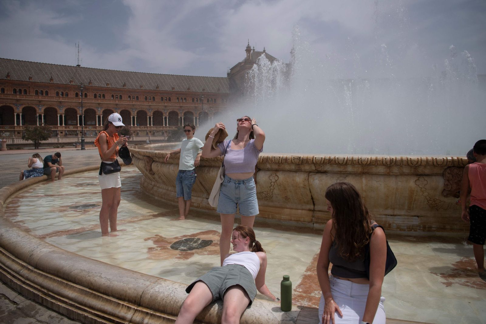 People cool off with a fountain's water during a heatwave in Seville on July 12, 2022. - Firefighters battled wildfires in Spain and Portugal as Western Europe faced its second heatwave in less than a month which threatened glaciers in the Alps and worsened drought conditions. The mass of hot air which pushed temperatures above 40 degrees Celsius (104 Fahrenheit) in large parts of the Iberian Peninsula was set to spread to the north and east in the coming days. (Photo by JORGE GUERRERO / AFP) - AFP