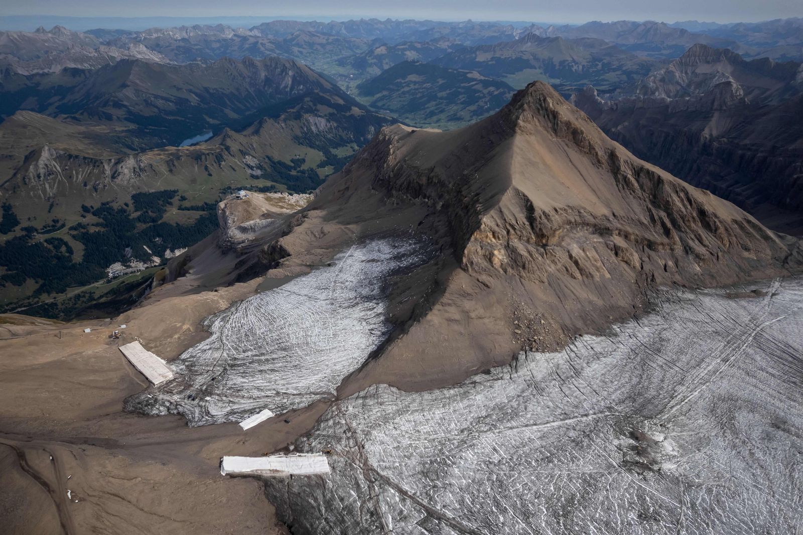 This aerial picture taken on September 13, 2022 at Glacier 3000 resort above Les Diablerets shows the Tsanfleuron pass free of the ice that covered it for at least 2,000 years next to blankets covering snow from the last winter season to prevent it from melting. - The thick layer of ice that has covered a Swiss mountain pass between Scex Rouge glacier and Tsanfleuron glacier since at least the Roman era has melted away completely. Following a dry winter, the summer heatwaves hitting Europe have been catastrophic for the Alpine glaciers, which have been melting at an accelerated rate. (Photo by Fabrice COFFRINI / AFP) - AFP