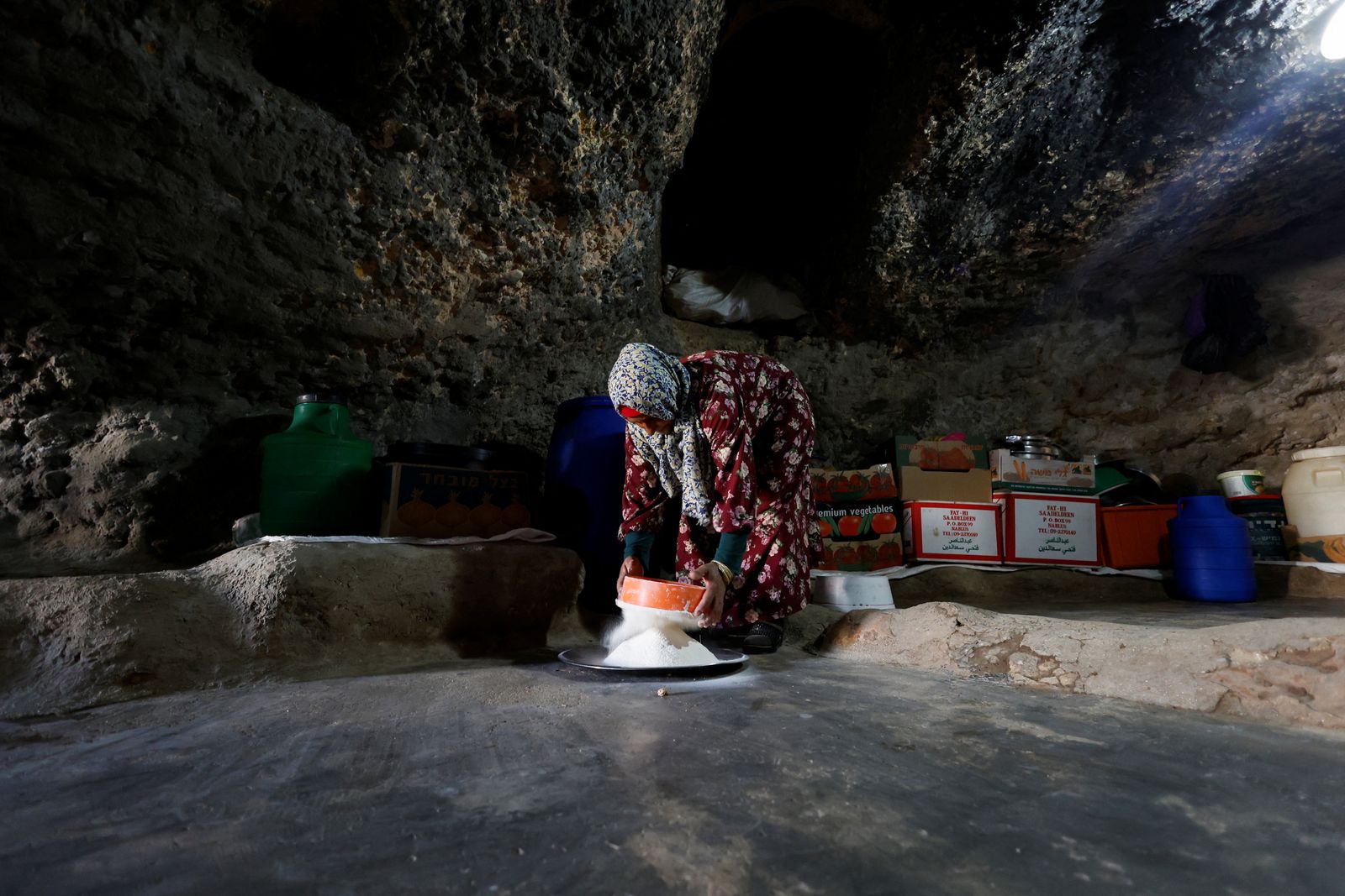 امرأة فلسطينية تنخل الدقيق في الكهف الذي تعيش فيه بعد أن رفضت المحكمة العليا الإسرائيلية التماساً ضد إخلاء أكثر من 1000 فلسطيني من المنطقة، مسافر يطا، جنوب الخليل، الضفة الغربية المحتلة - 7 مايو 2022. - REUTERS