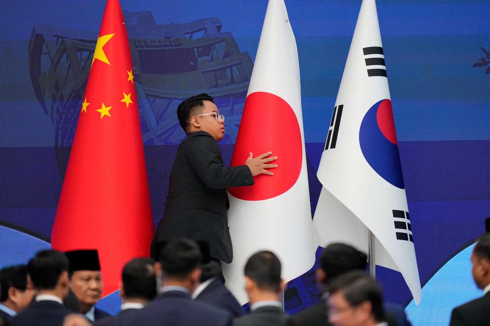 A staff member organises flags of China, Japan and Korea before the start of the 28th ASEAN Plus Three Summit in Kuala Lumpur, Malaysia, Monday, Oct. 27, 2025.       Vincent Thian/Pool via REUTERS