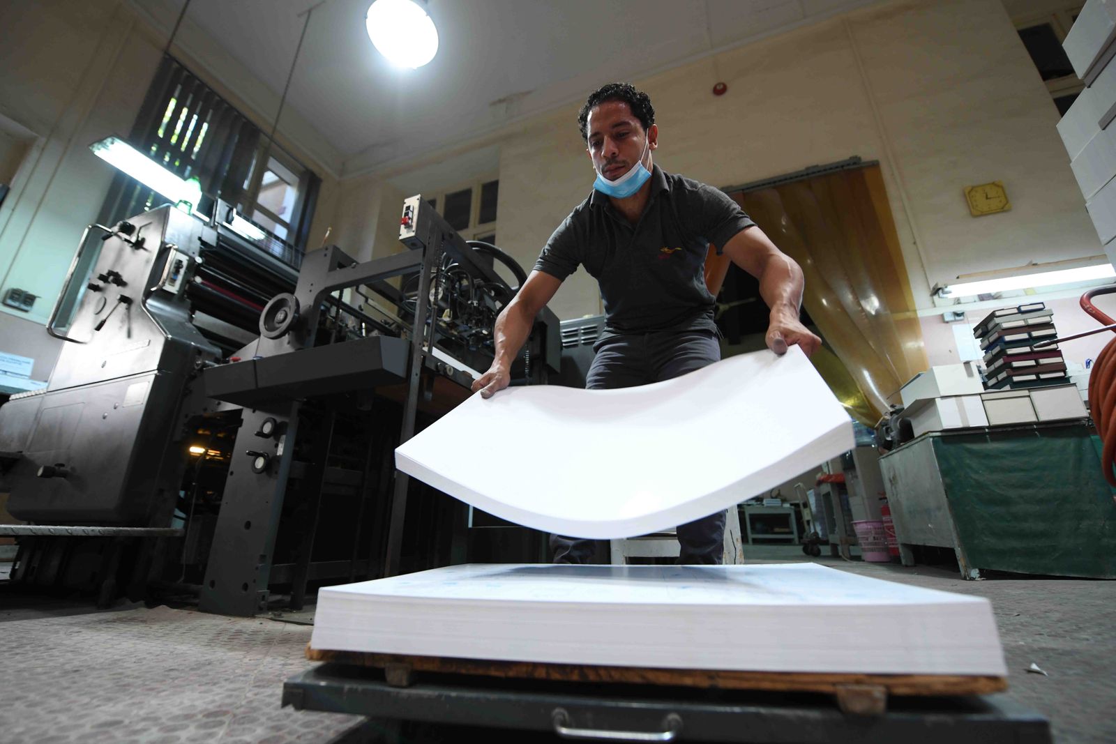 A man handles paper near a machine which allows the printing of ancient Egyptian inscriptions at the French Institute of Oriental Archaeology in Cairo on December 10, 2020. - The French-made typecasting machine is over a century old, the Egyptian hieroglyphs 5,000 years. Now, in a Cairo workshop, the mechanical marvel has come to life once again. Out of action for about three decades, a massive Foucher hot metal typecaster built in 1902 has been restored to its former glory. (Photo by Ahmad HASSAN / AFP) - AFP