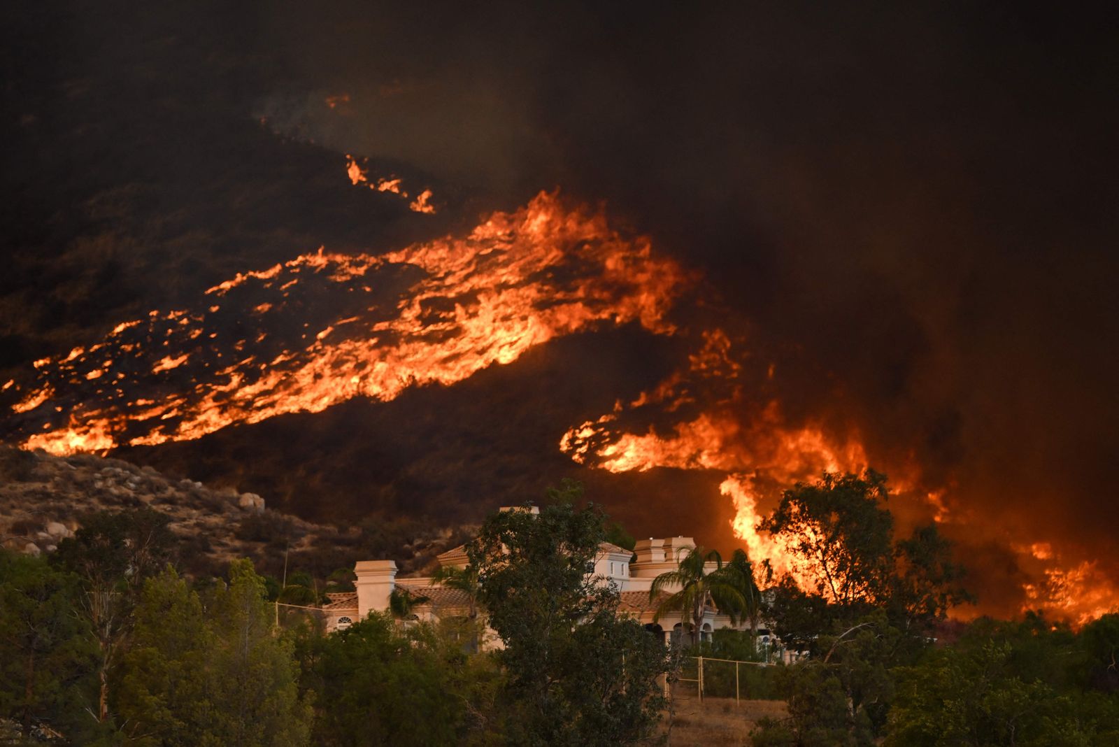 Plumes of smoke rise as wildfire approaches a home during the Fairview Fire near Hemet, California in Riverside County on September 7, 2022. - A ferocious heat wave scorching the western United States could finally begin to wane in the coming days, forecasters said on September 7, but they warned of dangerous fire conditions as howling winds sweep through the bone-dry region. (Photo by Patrick T. FALLON / AFP) - AFP