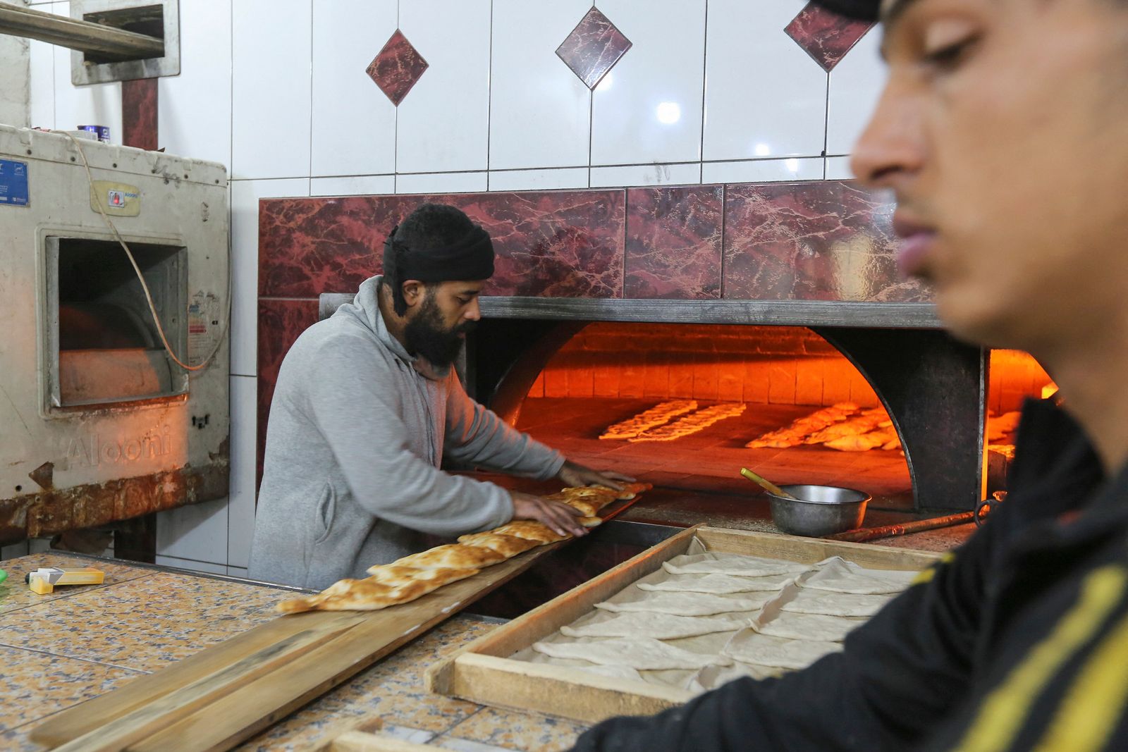 عمال في مخبز متخصص بالصمون العراقي بالعاصمة بغداد خلال عملية وضع الخبز في الفرن- 14 يناير 2023 - AFP