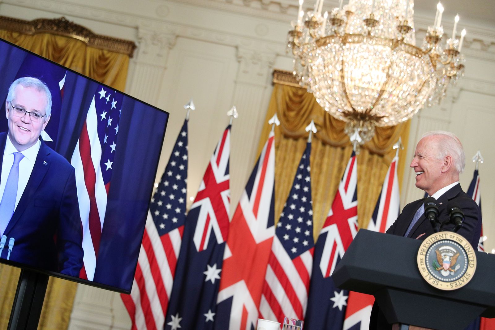 الرئيس الأميركي جو بايدن يبتسم خلال القمة الافتراضية مع رئيس الوزراء الأسترالي سكوت موريسون، الظاهر في الشاشة، ورئيس الوزراء البريطاني بوريس جونسون، في البيت الأبيض - 15 سبتمبر 2021 - REUTERS