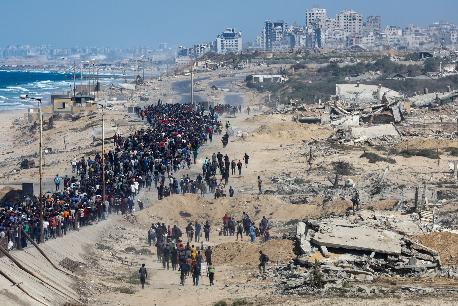 Palestinians, who were displaced to the southern part of Gaza at Israel's order during the war, walk along a road ast destroyed buildings as they attempt to return to the north after a ceasefire between Israel and Hamas in Gaza went into effect, in the central Gaza Strip, October 10, 2025. REUTERS/Mahmoud Issa