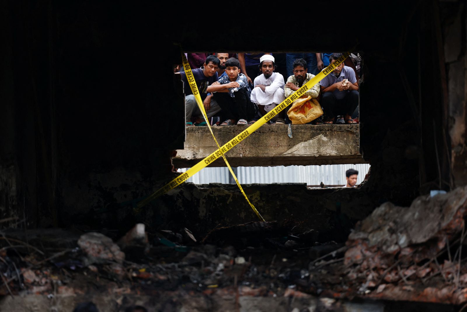 On lookers watch the site through a damaged window, after an air force training aircraft crashed into a building belong to Milestone School and College campus, in Dhaka, Bangladesh, July 22, 2025. REUTERS/Mohammad Ponir Hossain