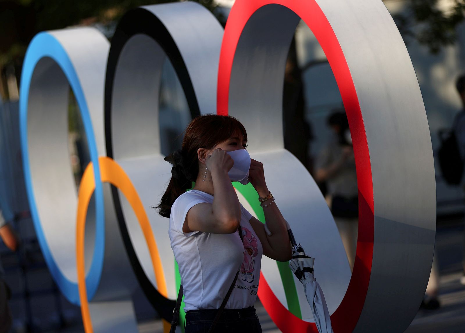 سيدة ترتدي كمامة وتسير أمام شعار الألعاب الأولمبية، في الملعب الوطني لطوكيو، اليابان. 31 يوليو 2021. - REUTERS