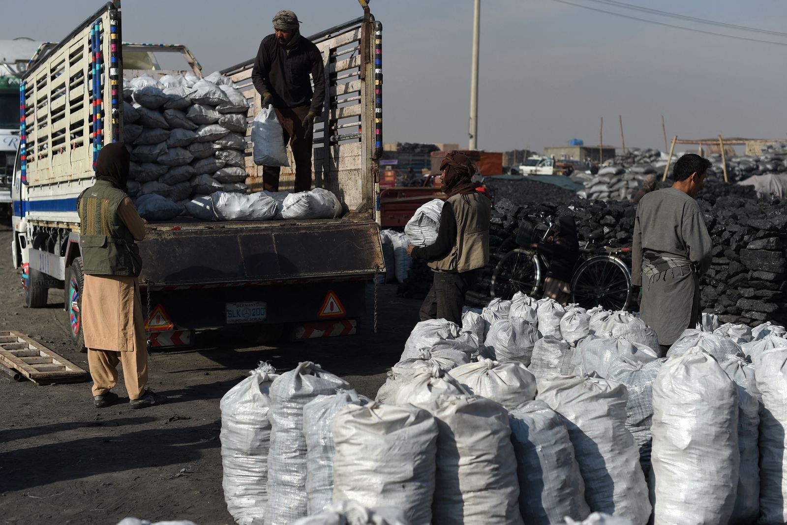 This photo taken on November 17, 2021 shows day labourers loading coal from a truck at a coal yard on the outskirts of Kabul. - Even as prices rise, Afghans have few options but to burn coal for heat, creating some of the world's most dangerous air. (Photo by WAKIL KOHSAR / AFP) / TO GO WITH Afghanistan-energy-economy-coal-environment,FOCUS by Caroline TAIX - AFP