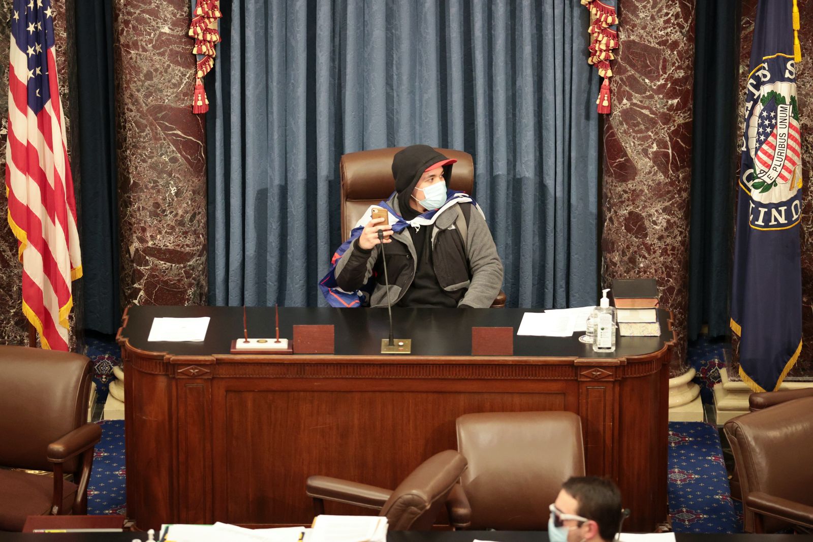 متظاهر من أنصار الرئيس ترمب يجلس على مقعد رئيس مجلس الشيوخ الأميركي خلال اقتحام أنصار ترمب للكونغرس - AFP