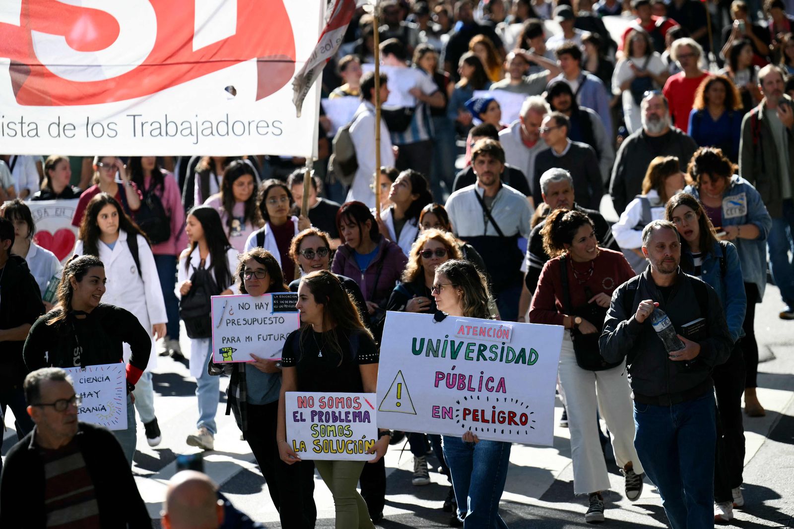 A demonstrator (R) holds a sign that reads 'Attention, public university in danger' during a march in protest of the budget adjustment to public universities in Buenos Aires on April 23, 2024. Thousands of university students took to the streets of Argentina on Tuesday to repudiate the defunding of the public university, which was declared in a state of budgetary emergency in the framework of the adjustment policy of the right-wing president Javier Milei. (Photo by Luis ROBAYO / AFP)