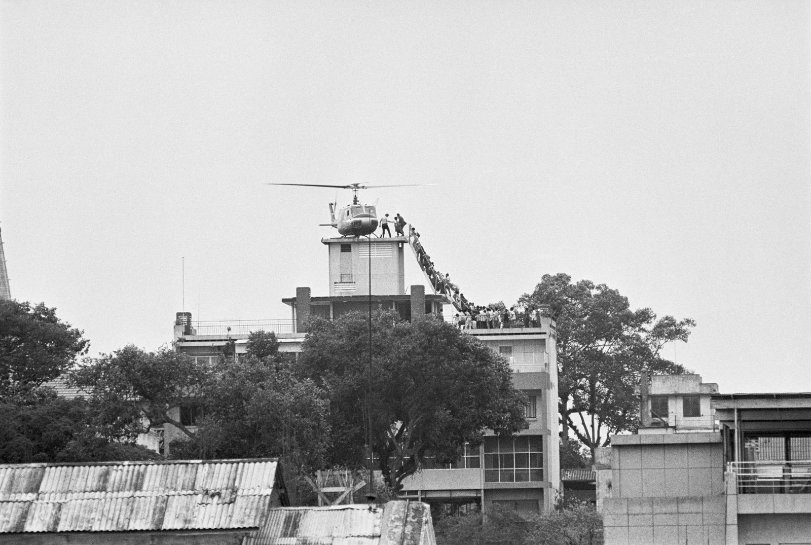 عنصر في وكالة الاستخبارات المركزية الأميركية يساعد فيتناميين لدى إجلائهم إلى مروحية على سطح مبنى في سايغون - 29 أبريل 1975 - Getty