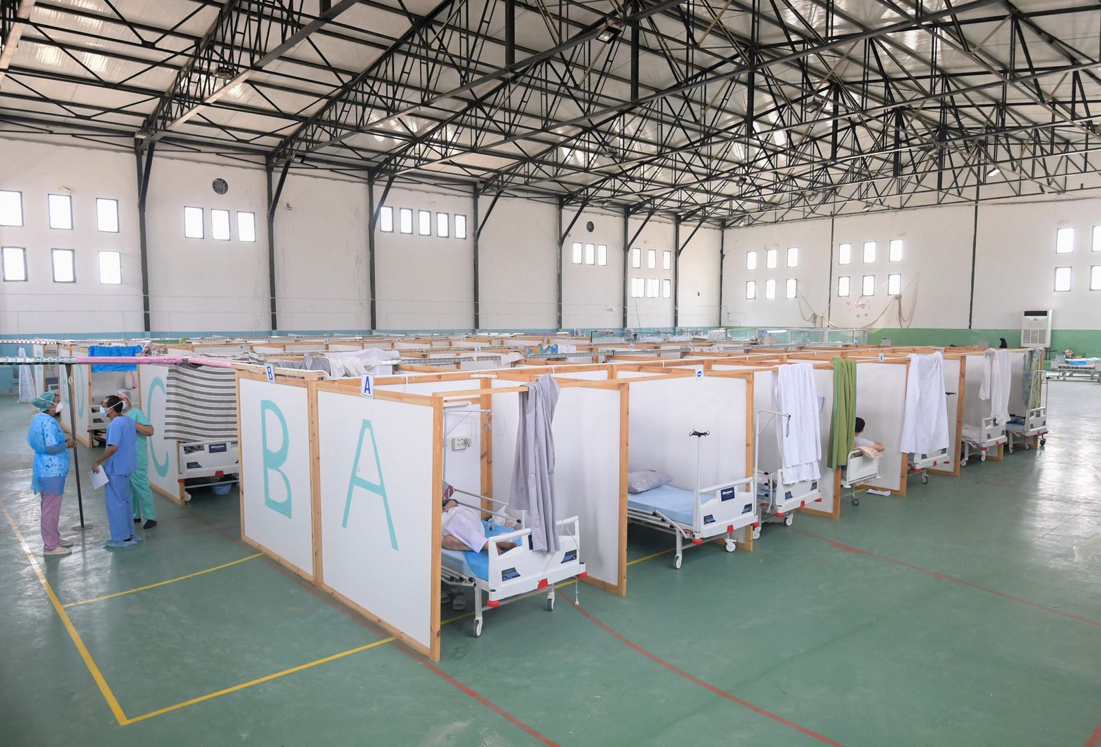 Tunisian doctors are stand next to rows of patients at a gym that was converted to deal with a surge in new COVID-19 infections in the east-central city of Kairouan on July 4, 2021. - Tunisia placed the capital Tunis and the northern town of Bizerte under a partial lockdown from until July 14 in a bid to rein in record daily coronavirus cases and deaths. (Photo by FETHI BELAID / AFP) - AFP