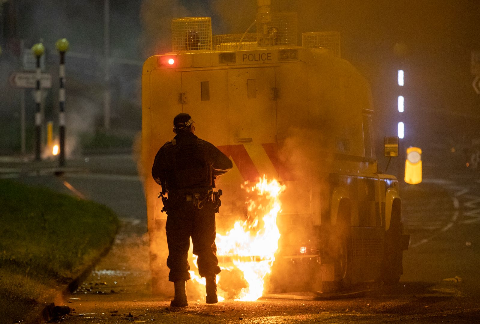 ضابط يسير خلف سيارة للشرطة تتصاعد فيها ألسنة اللهب وذلك على خلفية اندلاع أعمال عنف في منطقة نيوتاونبي، شمال بلفاست، في إيرلندا الشمالية - AFP