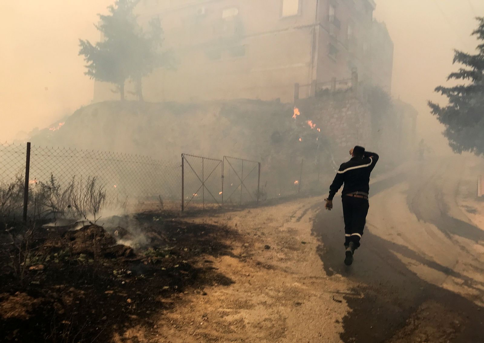 عامل إنقاذ يسير بالقرب من الدخان المتصاعد من حريق غابة في ولاية تيزي وزو الجبلية، شرق الجزائر العاصمة، الجزائر. 10 أغسطس 2021. - REUTERS