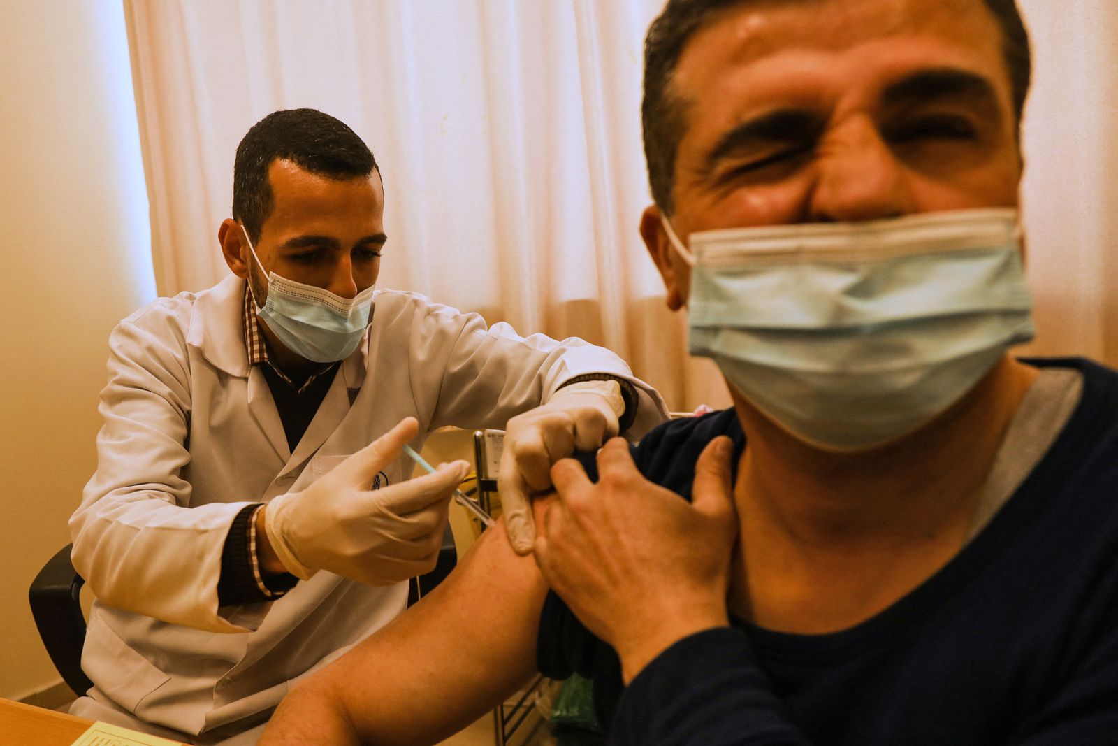 موظف في وكالة الأمم المتحدة لإغاثة وتشغيل لاجئي فلسطين (الأونروا) يعطي لقاح كورونا لأحد أفراد الطاقم الطبي في مدينة غزة ، - AFP
