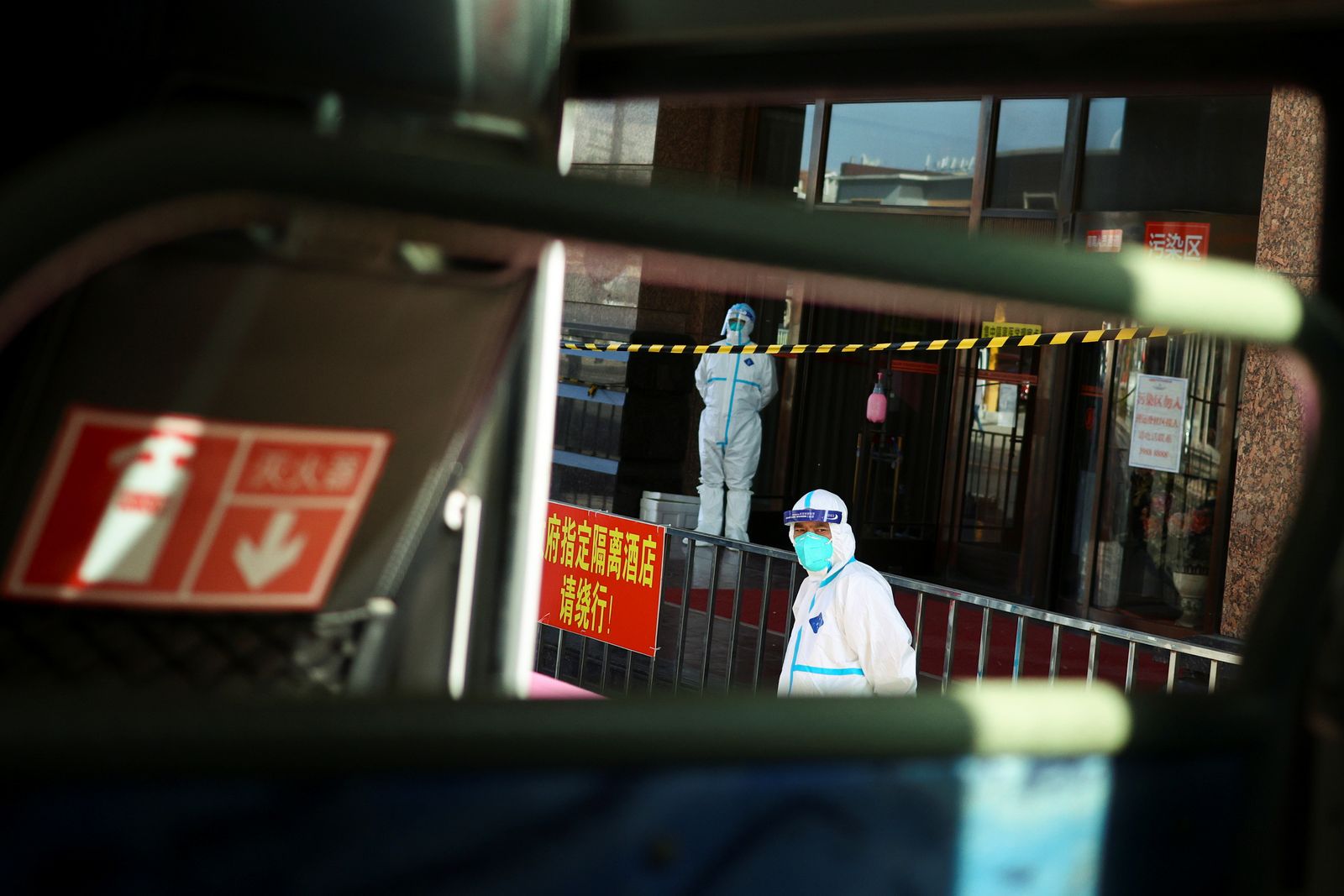 Staff members in protective suits stand outside a quarantine hotel in Dalian - REUTERS