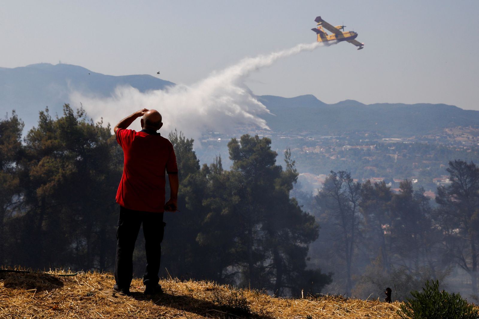 رجل يشاهد طائرة تساهم في إخماد حرائق في اليونان. 27 يوليو 2021 - REUTERS