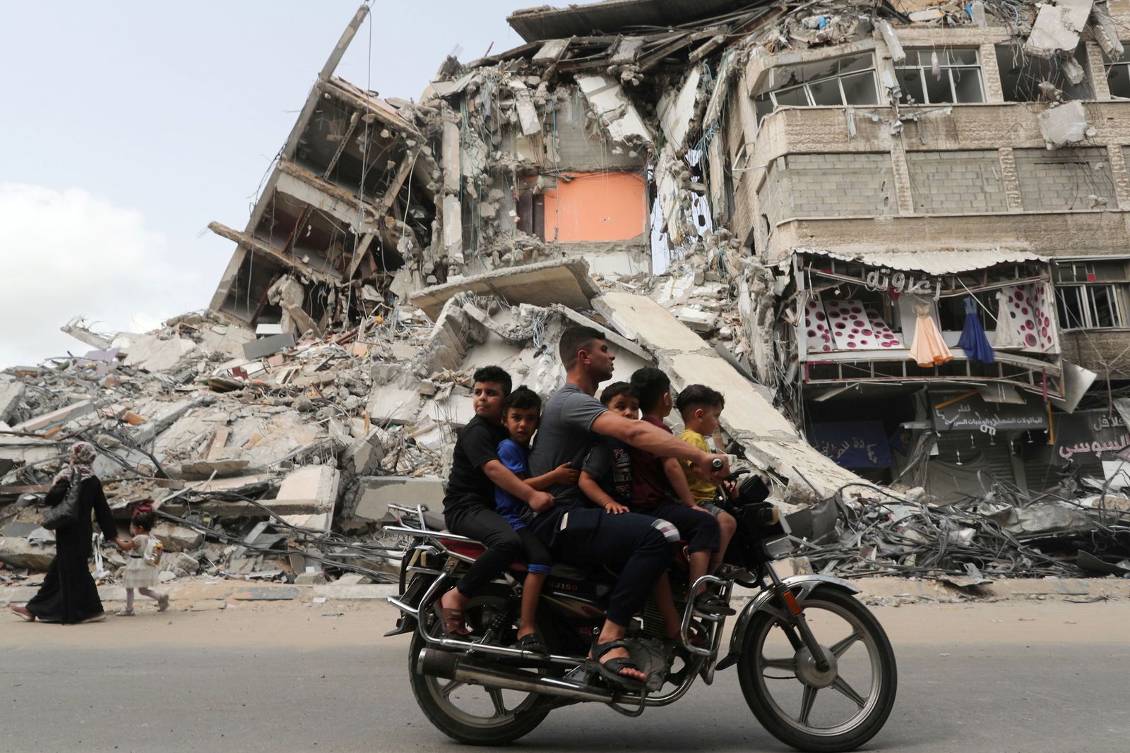 فلسطينيون يركبون دراجة نارية يمرون أمام مبنى دمرته غارة إسرائيلية في غزة- 21 مايو 2021 - REUTERS