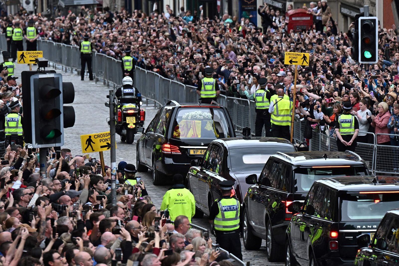 Members of the public watch the hearse carrying the coffin of Queen Elizabeth II, draped in the Royal Standard of Scotland, as it is driven through Edinburgh towards the Palace of Holyroodhouse, on September 11, 2022. - The coffin carrying the body of Queen Elizabeth II left her beloved Balmoral Castle on Sunday, beginning a six-hour journey to the Scottish capital of Edinburgh. (Photo by Oli SCARFF / AFP) - AFP