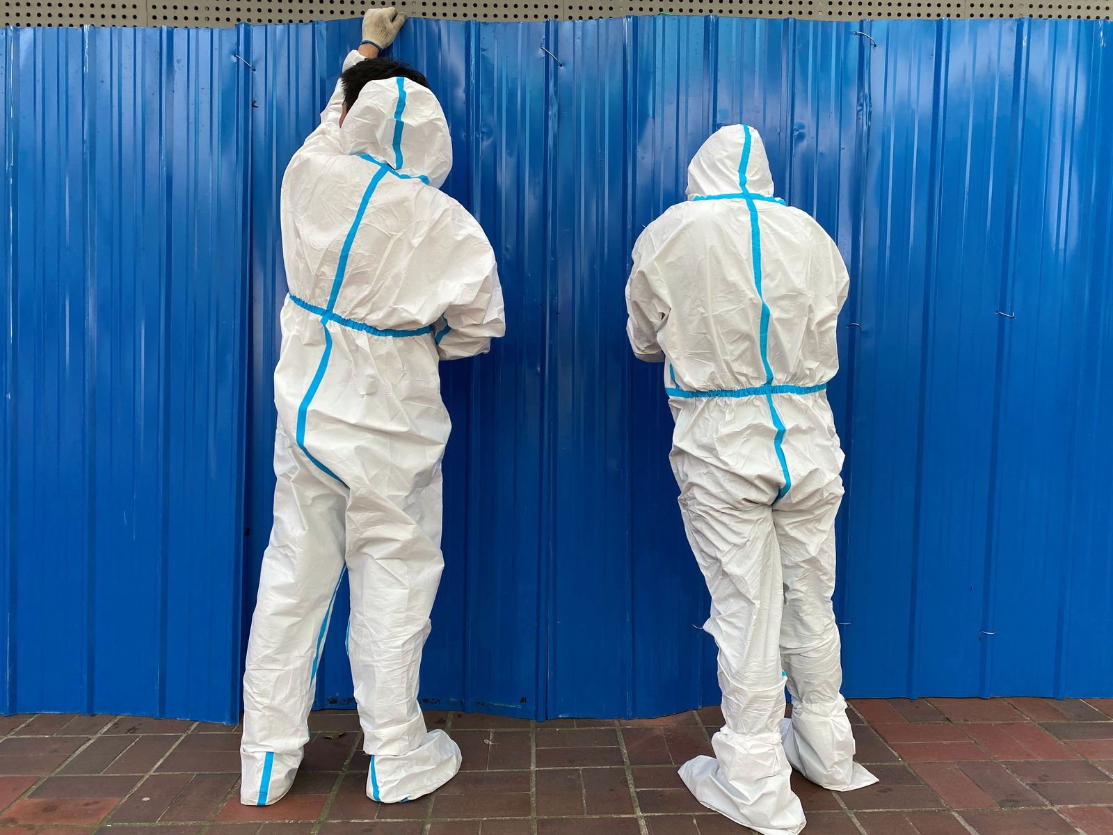 عاملان يرتديان الملابس الواقية يقيمان حواجز خارج مبنى في أعقاب تفشي مرض كورونا في شنغهاي. 9 يونيو 2022 - REUTERS