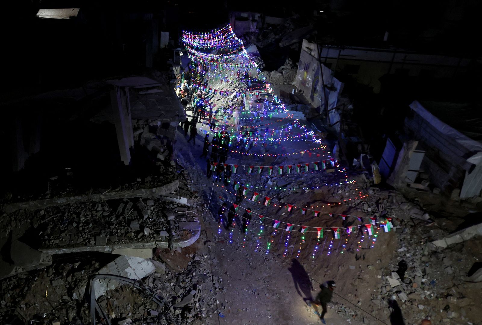 Palestinians walk under decorative lights and near the rubble of buildings, ahead of the holy fasting month of Ramadan, amid a ceasefire between Israel and Hamas, in Khan Younis, in the southern Gaza Strip, February 27, 2025. REUTERS/Ramadan Abed