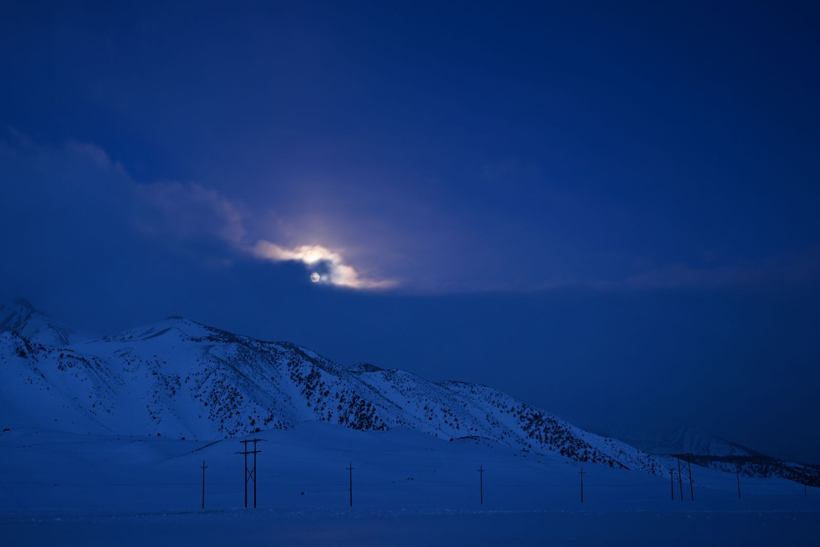 The moon sets behind clouds as snow is seen on the mountains of the Eastern Sierras near Convict Lake along Highway 395 after record snowpack from winter storms in Mono County, south of Mammoth Lakes, California on April 7, 2023. - The LA aqueduct, built and operated by the Los Angeles Department of Water and Power (LADWP), delivers water from the Owens River in the Eastern Sierra Nevada Mountains to Los Angeles, impacting communities and the environment in the Owens Valley. (Photo by Patrick T. Fallon / AFP) - AFP