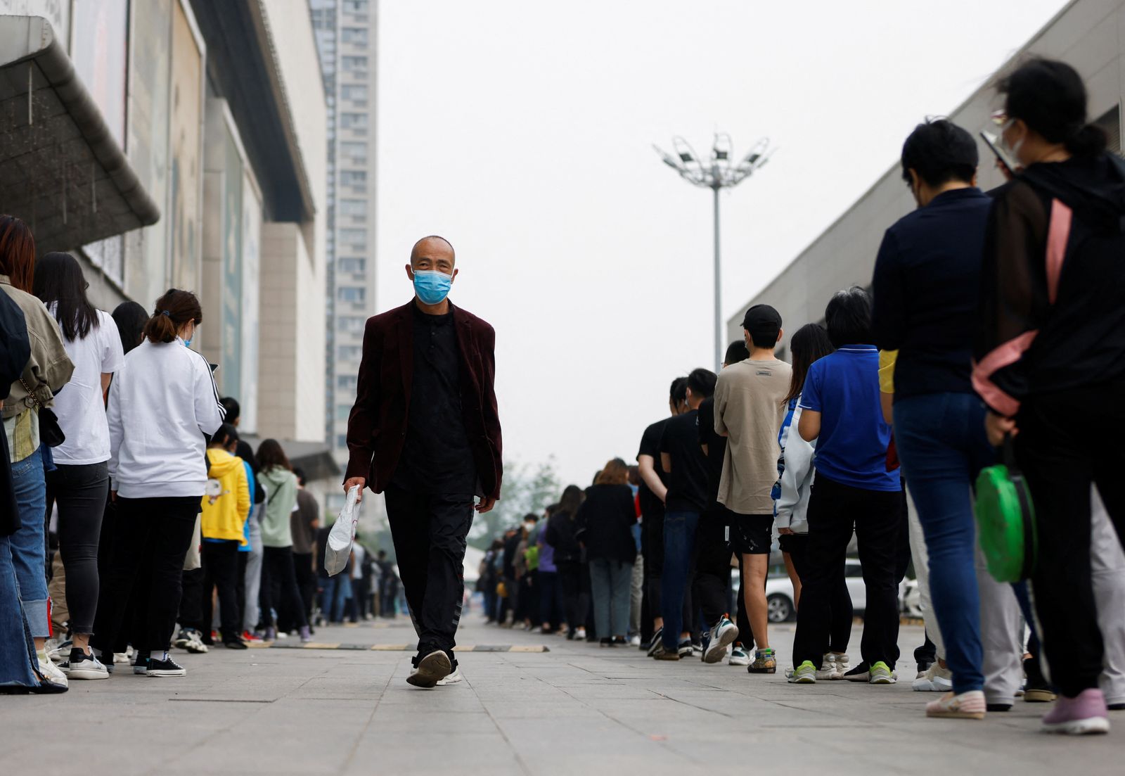 A man wearing a face mask walks next to people lining up to take nucleic acid tests at a makeshift testing site following the coronavirus disease (COVID-19) outbreak in Beijing, China, April 25, 2022. REUTERS/Carlos Garcia Rawlins - REUTERS