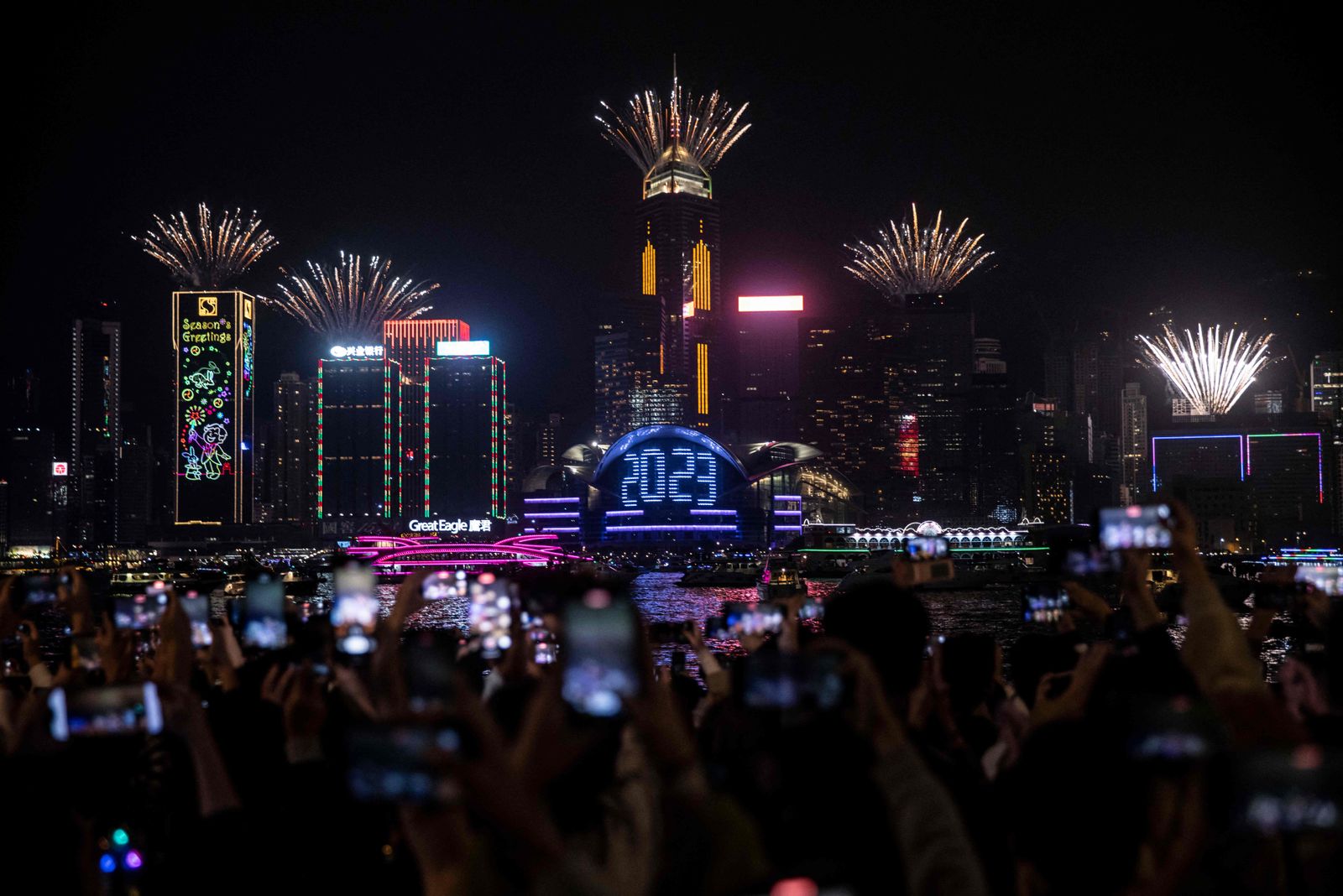 Revellers watch a fireworks and laser show as they celebrate the New Year next to Victoria Harbour in Hong Kong on January 1, 2023. (Photo by ISAAC LAWRENCE / AFP) - AFP