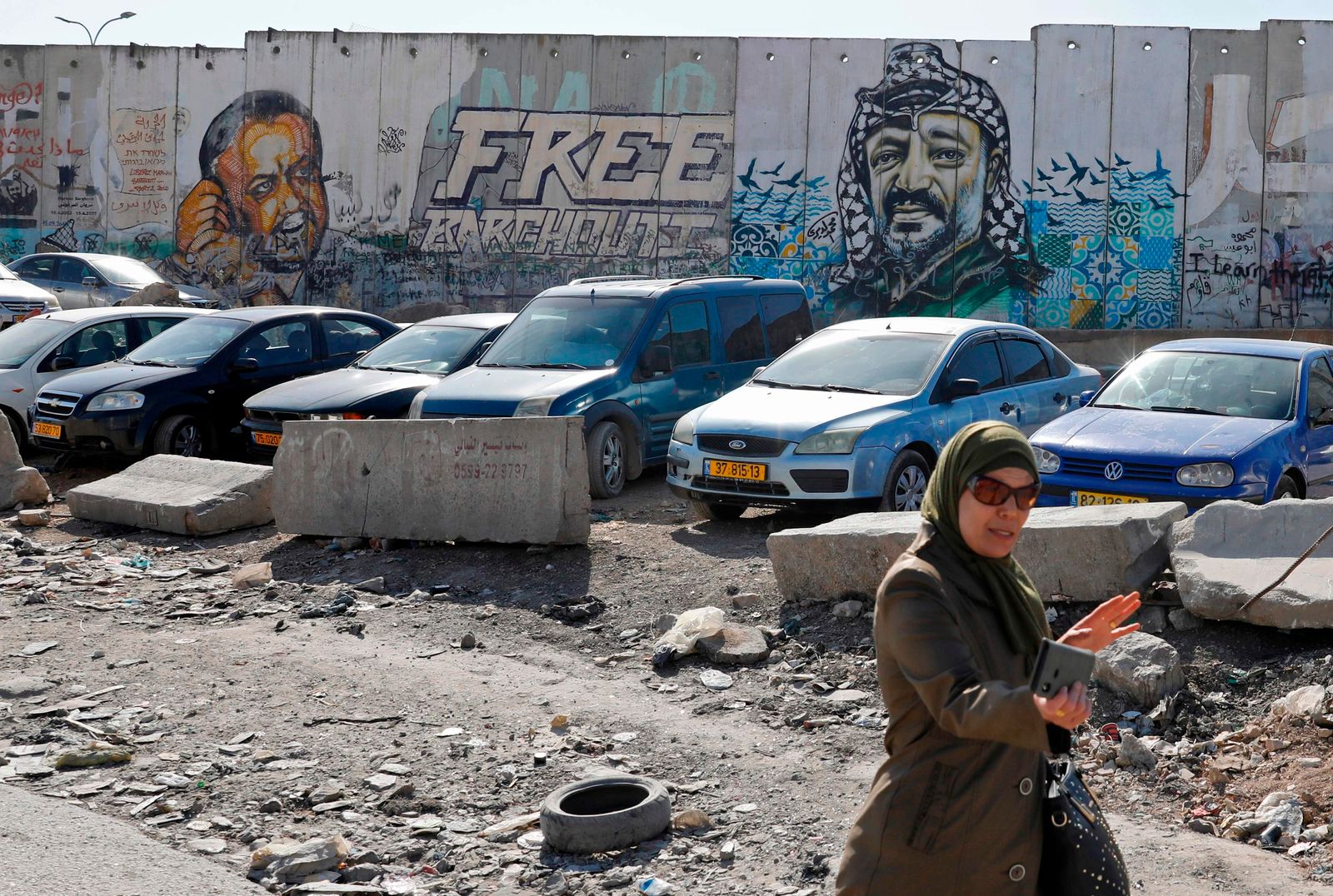 امرأة تسير أمام لوحة جدارية تحمل صورة عملاقة للزعيم الفلسطيني الراحل ياسر عرفات (إلى اليمين) على جزء من الجدار العازل الإسرائيلي المثير للجدل عند حاجز قلنديا ، بين القدس ورام الله ، 11 نوفمبر ، 2019 بينما يحتفل الفلسطينيون بالذكرى الخامسة عشرة للوفاة رئيسهم السابق. - تظهر الصورة الأخرى زعيم فتح المسجون مروان البرغوثي (إلى اليسار). (تصوير أحمد غرابلي / وكالة الصحافة الفرنسية) - AFP