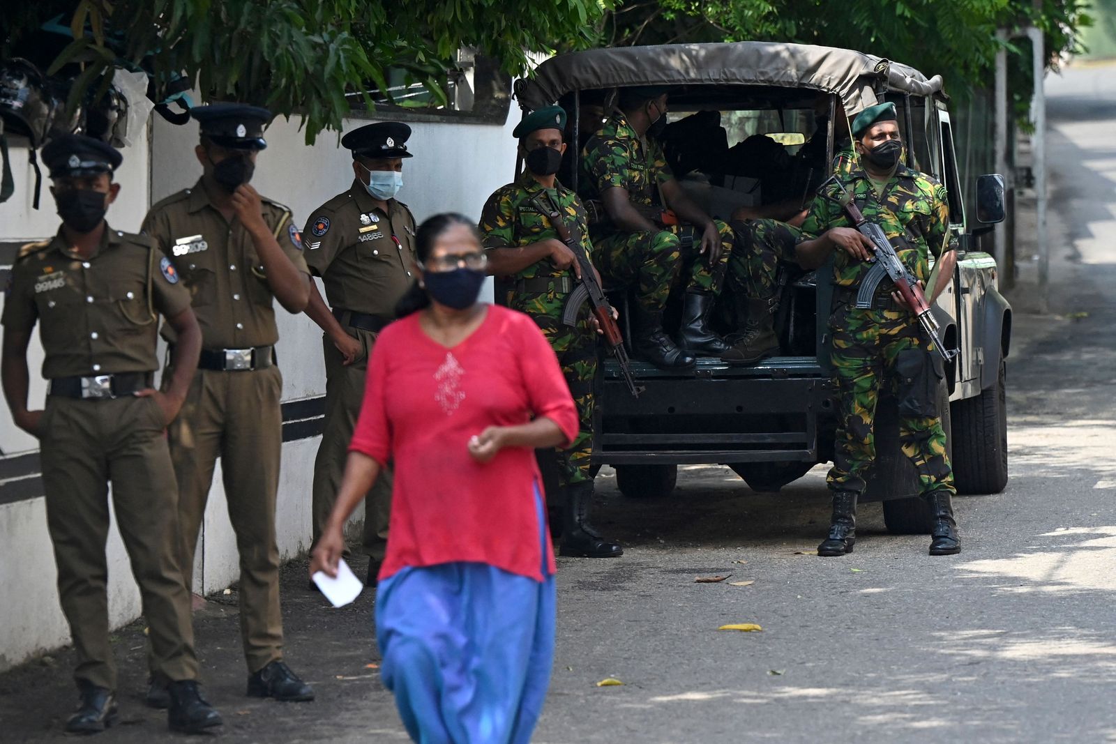 A pedestrian walks past Special Task Force (STF) and police personnel standing on guard along a street in Colombo on April 2, 2022. - Troops armed with sweeping powers to detain suspects were deployed in Sri Lanka, hours after the president declared a state of emergency as protests against him escalated. (Photo by Ishara S. KODIKARA / AFP) - AFP