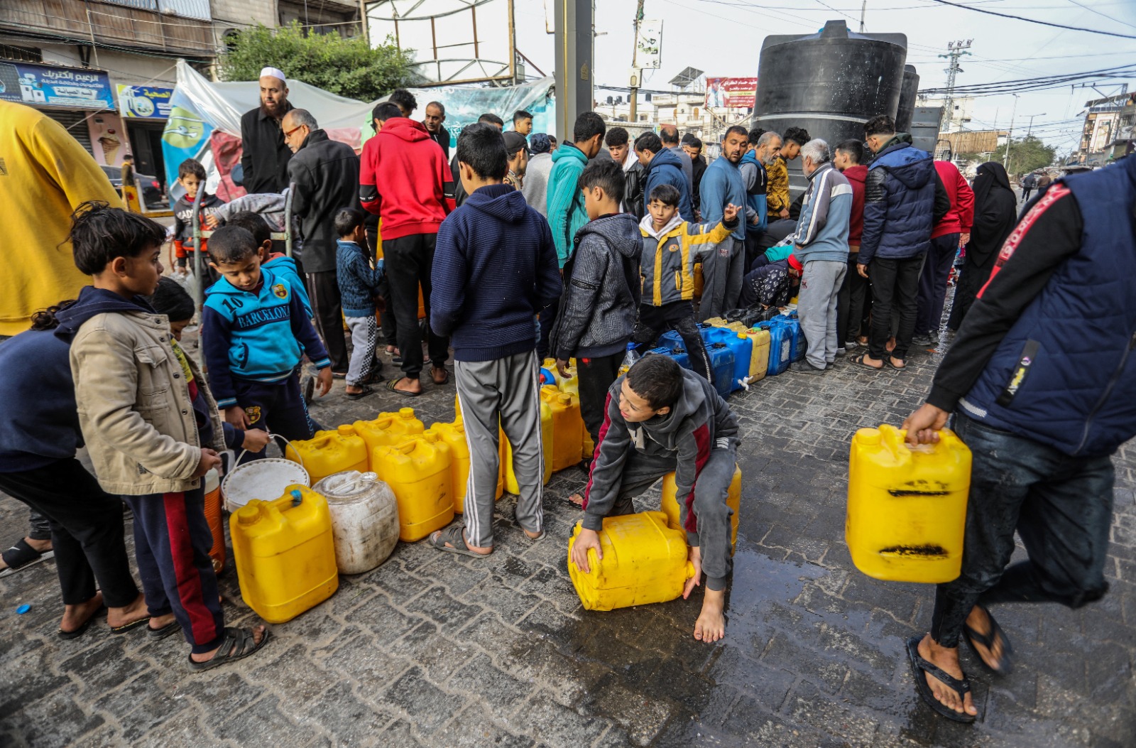 ينتظر الفلسطينيون والأطفال في طابور لتلبية احتياجاتهم من المياه من الخزانات المتنقلة بسبب الأضرار الكبيرة التي لحقت بالبنية التحتية في رفح، غزة في 23 ديسمبر 2023