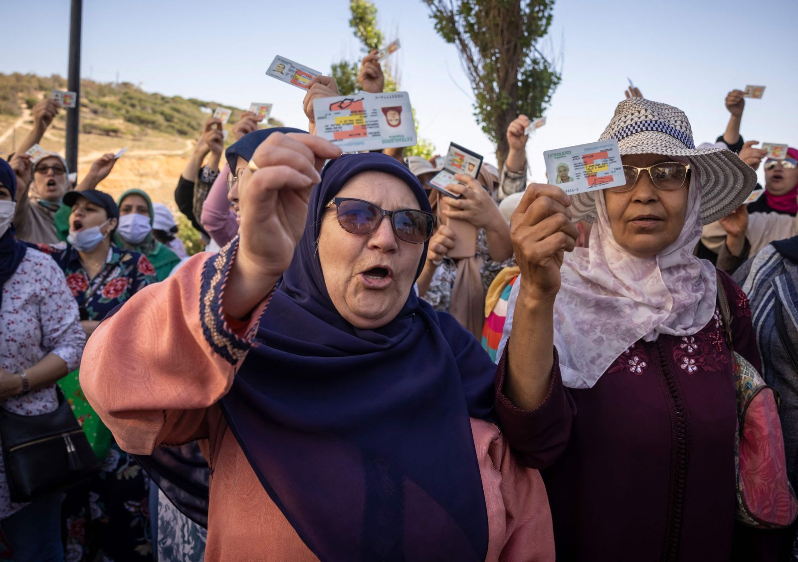 Moroccan workers gather with their work permits during a demonstration demanding the right to access the Spanish enclave of Ceuta without a visa, at Morocco's Fnideq border post on May 31, 2022. - Morocco and Spain have reopened the land borders between the north African country and the Spanish enclaves of Ceuta and Melilla, two years after they were shut due to Covid restrictions and a major diplomatic row. The reopening of the borders of the two enclaves initially remains limited to residents of Europe's open-borders Schengen area and their family members. (Photo by FADEL SENNA / AFP) - AFP