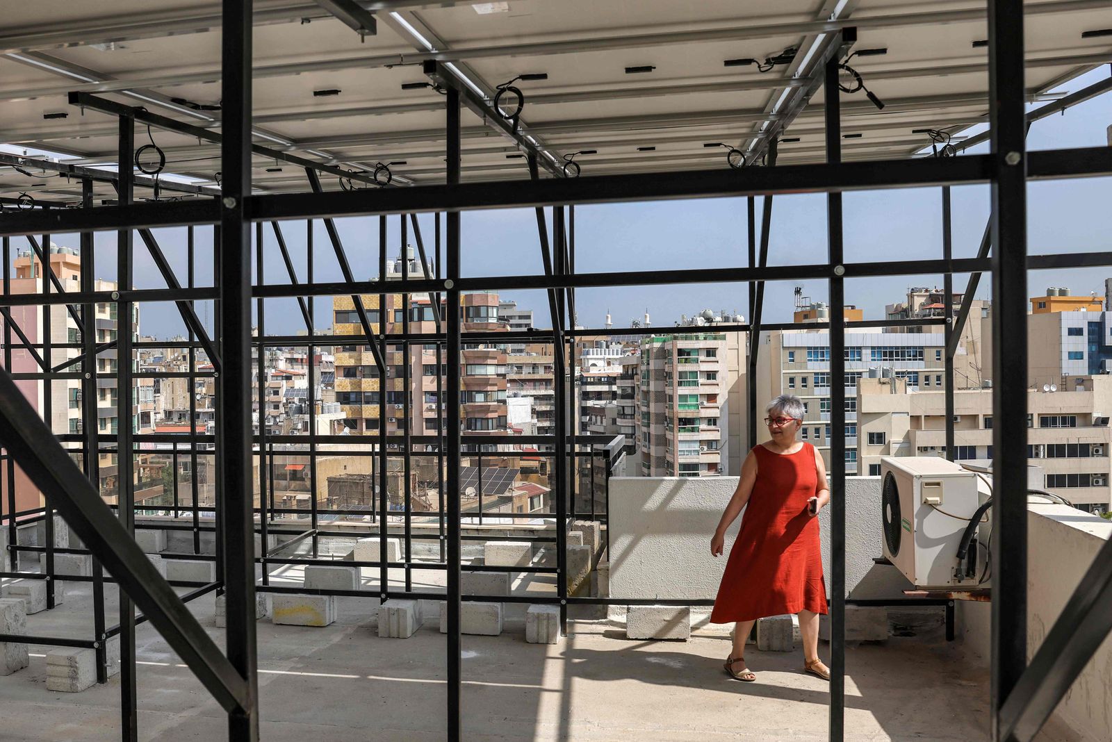 Lebanese homemaker Zeina Sayegh walks beneath the solar powers she installed atop her apartment building the in Lebanon's capital Beirut on August 29, 2022, which were installed the previous year after the government lifted most fuel subsidies and generator-produced power became unattainable. - Lebanon's economy collapsed in 2019 after decades of corruption and mismanagement, leaving the state unable to provide electricity for more than an hour or two. Last winter, the mountain village barely had three hours of daily generator electricity. Solar power now helps keep the lights on for 17 hours, an engineer working on the project said, providing a semblance of normality. (Photo by JOSEPH EID / AFP) - AFP