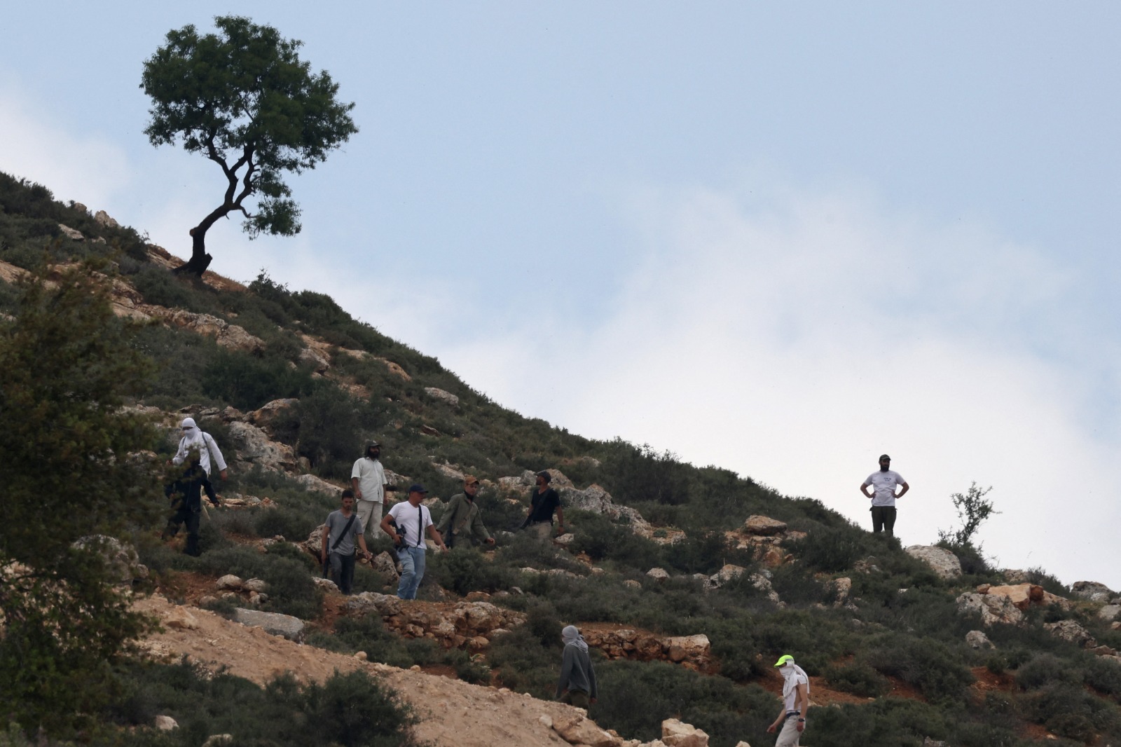 مستوطنون إسرائيليون مسلحون يتجمعون على تلة تطل على قرية المغير بالقرب من رام الله بعد مهاجمتها. 13 أبريل 2024