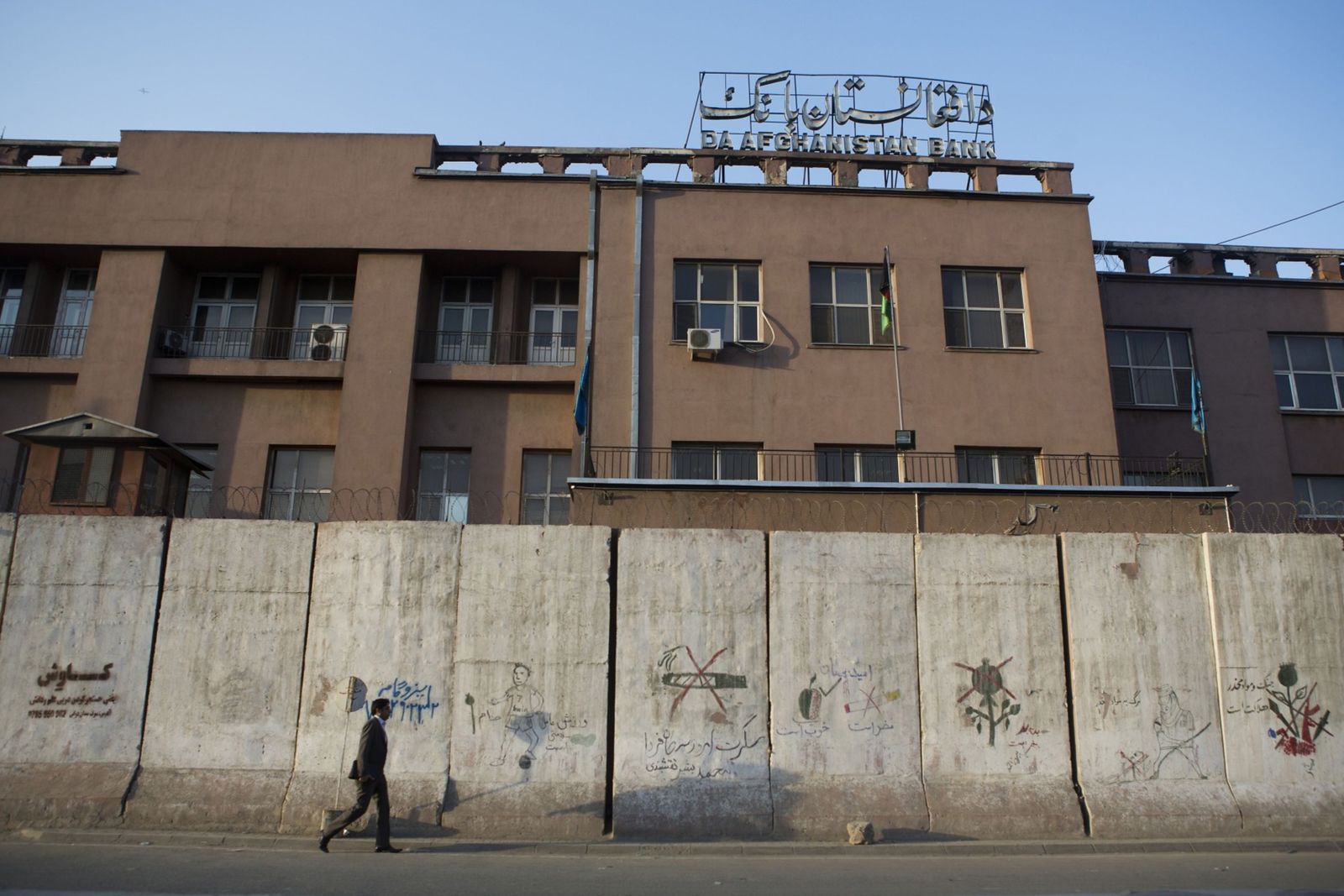 يمرّ قرب جدار أمام مقرّ المصرف المركزي الأفغاني في كابول - 6 أغسطس 2013 - Bloomberg