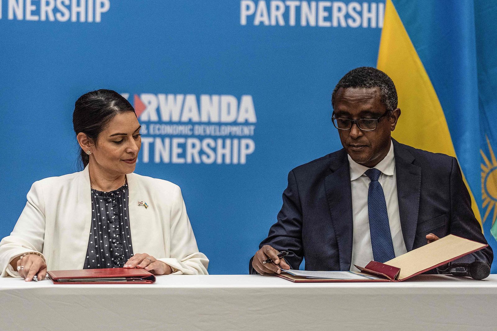 British Home Secretary Priti Patel (L), and Rwandan Minister of Foreign Affairs and International Cooperation Vincent Biruta, sign an agreement at Kigali Convention Center, Kigali, Rwanda on April 14, 2022. - An agreement was finally announced Thursday with Rwanda, where British Home Secretary Priti Patel visited. Asylum seekers arriving in the UK will be sent to Rwanda, under a controversial deal announced Thursday with which Boris Johnson's government hopes to deter record-breaking illegal Channel crossings. London will initially finance the device to the tune of 120 million pounds sterling (144 million euros). (Photo by Simon WOHLFAHRT / AFP) - AFP