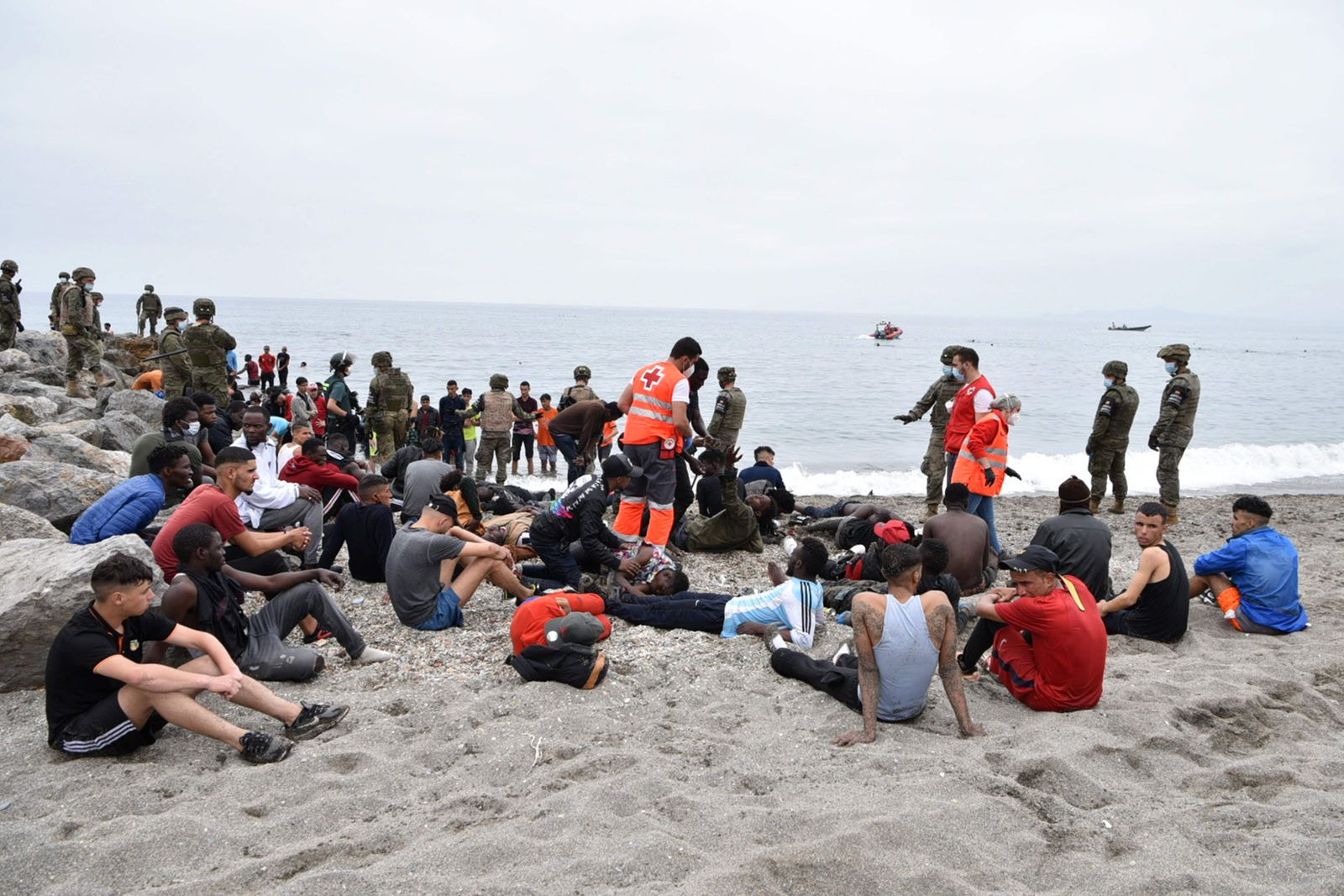 Red Cross members assist migrants who arrived swimming at the Spanish enclave of Ceuta as Spanish soldiers and Guardia Civil members stand guard on May 18, 2021 in Ceuta. - Spain has returned to Morocco nearly half of the 6,000 migrants who entered its Ceuta enclave, as hundreds more tried to enter its other north African territory. (Photo by Antonio Sempere / AFP) - AFP