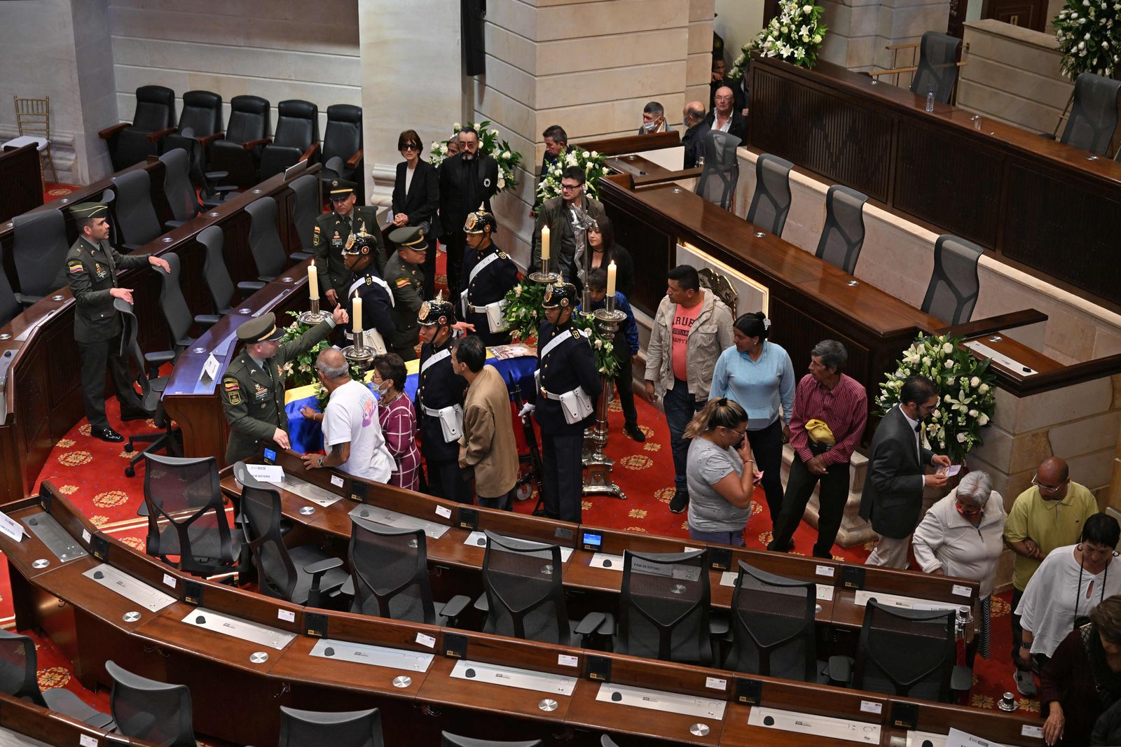 People pass by the coffin with the remains of Colombian painter and sculptor Fernando Botero, who died aged 91 on September 15, as he lies in state at the funeral chapel set at the Congress in Bogota, on September 22, 2023. The remains of Fernando Botero, who died aged 91 on September 15, will lie in wake in his home country before his burial in Italy, the artist's family said earlier this week. Known for his voluptuous depictions of people and animals using different media, Colombia's most famous artist died in Monaco, where he lived, after developing pneumonia. In a media statement, the Botero family said the artist's remains will be in the capital on Thursday before being moved to Medellin, where several events will be held to honor his memory. (Photo by Juan BARRETO / AFP)