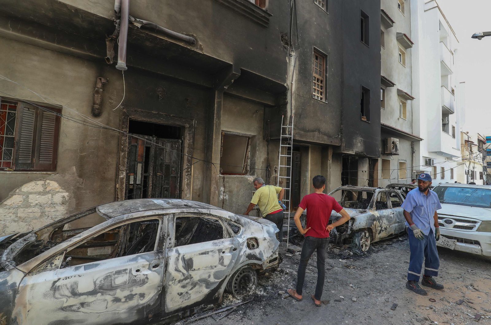 People inspect the damage following clashes between backers of rival governments in Libya's capital Tripoli, on August 28, 2022. - Flights resumed and shops re-opened in Libya's capital after clashes between backers of rival governments killed at least 32 people and sparked fears of major new conflict. (Photo by Mahmud TURKIA / AFP) - AFP