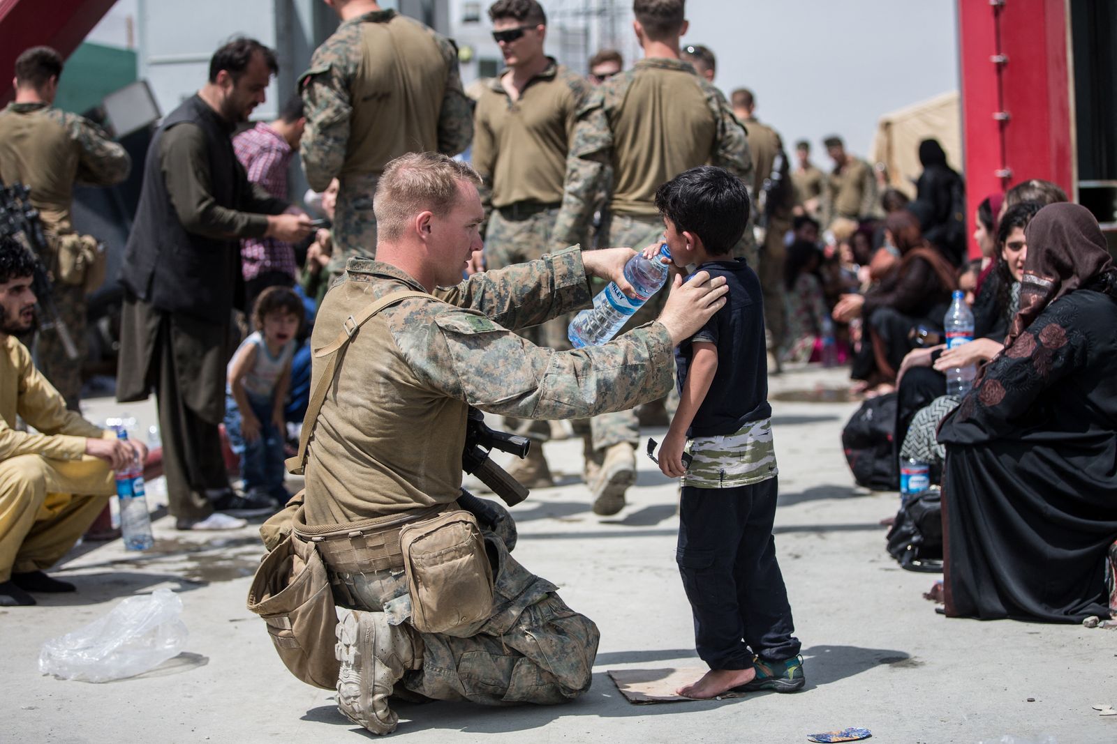 أحد أفراد مشاة البحرية الأميركية يسقي طفلاً أفغانياً مياه عذبة خلال عملية إجلاء في مطار حامد كرزاي الدولي في كابول - 20 أغسطس 2021 - AFP