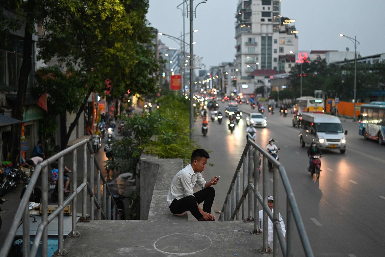 A man checks his smartphone while waiting at a sidewalk in Hanoi on April 6, 2021. (Photo by MANAN VATSYAYANA / AFP) - AFP