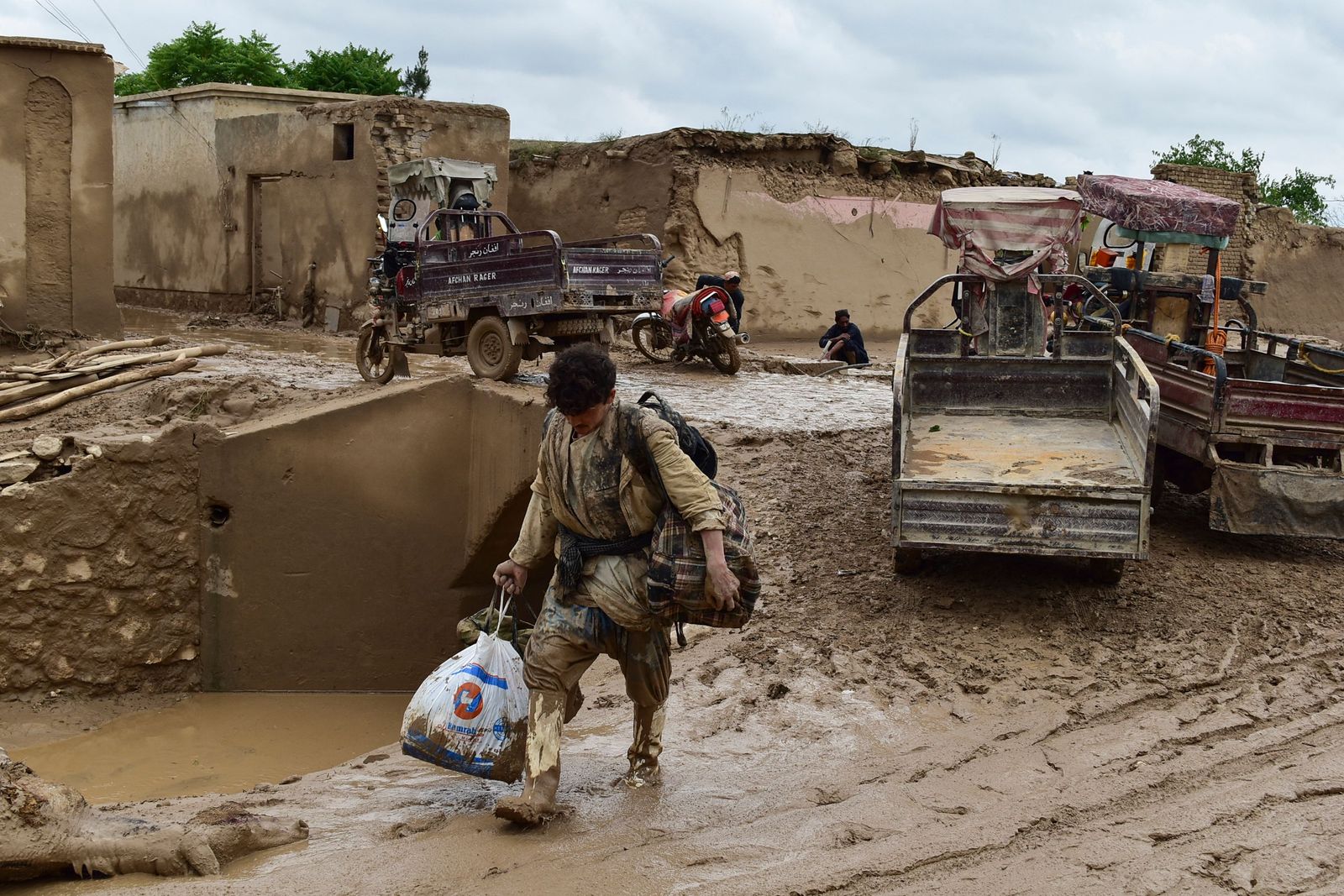 An Afghan man carries his belongings as he walks through a mud covered street following a flash flood after a heavy rainfall in Laqiha village of Baghlan-i-Markazi district in Baghlan province on May 11, 2024. At least 62 people, mainly women and children, were killed on May 10 in flash flooding that ripped through Afghanistan's Baghlan province, in the north of the country, a local official told AFP. (Photo by AFP)