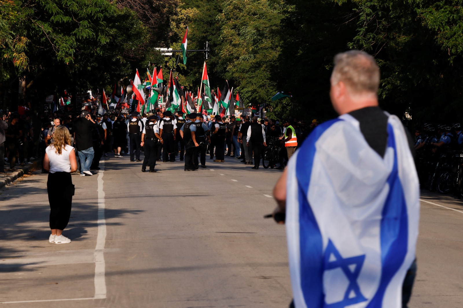 شخص يحمل العلم الإسرائيلي أمام متظاهرين داعمين للفلسطينيين خلال احتجاجات في شيكاجو بولاية إلينوي - REUTERS