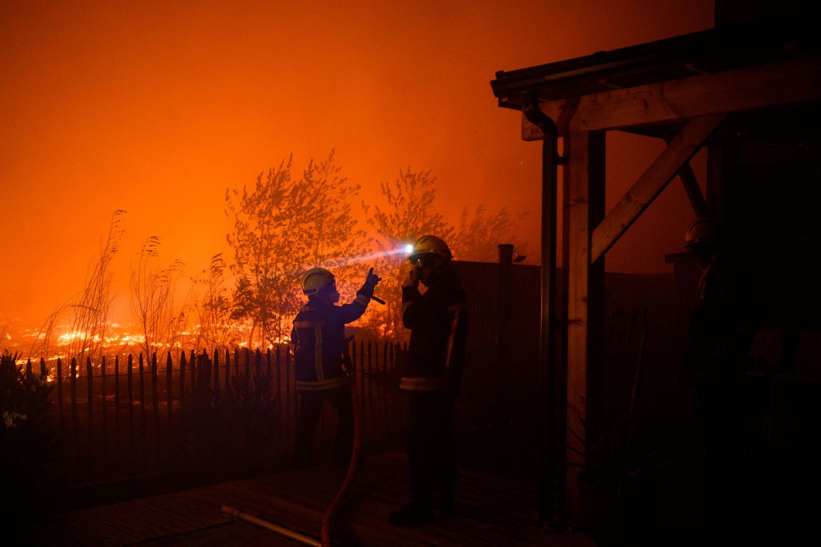 This photo taken late on September 12, 2022 shows firefighters at work to protect houses threatened by a wildfire in Saumos near Bordeaux, southwestern France. - A fire in progress since September 12, 2022 afternoon has covered 1300 hectares of vegetation and forest in Saumos and forced the evacuation of the town in a context of high temperatures in Gironde. (Photo by PHILIPPE LOPEZ / AFP) - AFP