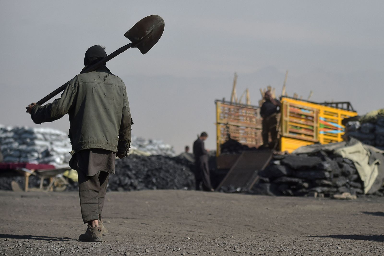 This photo taken on November 17, 2021 shows a day labourer carrying a shovel as he walks at a coal yard on the outskirts of Kabul. - Even as prices rise, Afghans have few options but to burn coal for heat, creating some of the world's most dangerous air. (Photo by WAKIL KOHSAR / AFP) / TO GO WITH Afghanistan-energy-economy-coal-environment,FOCUS by Caroline TAIX - AFP