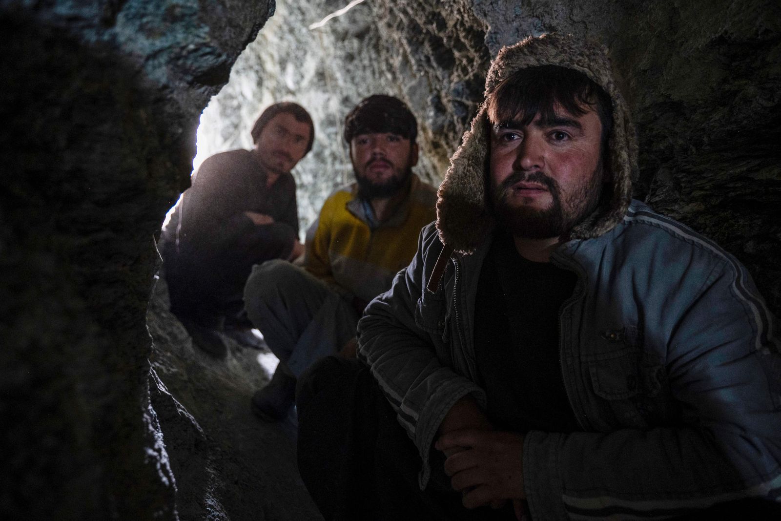 In this photograph taken on February 24, 2024, Afghan miners sit near the entrance of a gold mine tunnel in the mountains of Yaftal Sufla district in Badakhshan province. Tearing off a piece of mouldy flatbread, Homayon gulped tea in a brief reprieve from the din of the machines he and a dozen other men were using to dig for gold on a mountainside in northeastern Afghanistan.  The 30-year-old found little work as a mechanic in nearby Faizabad city, so he banded with other unemployed men to try their luck carving out a living in the rocky mountains that dominate Badakhshan province. (Photo by Wakil KOHSAR / AFP)