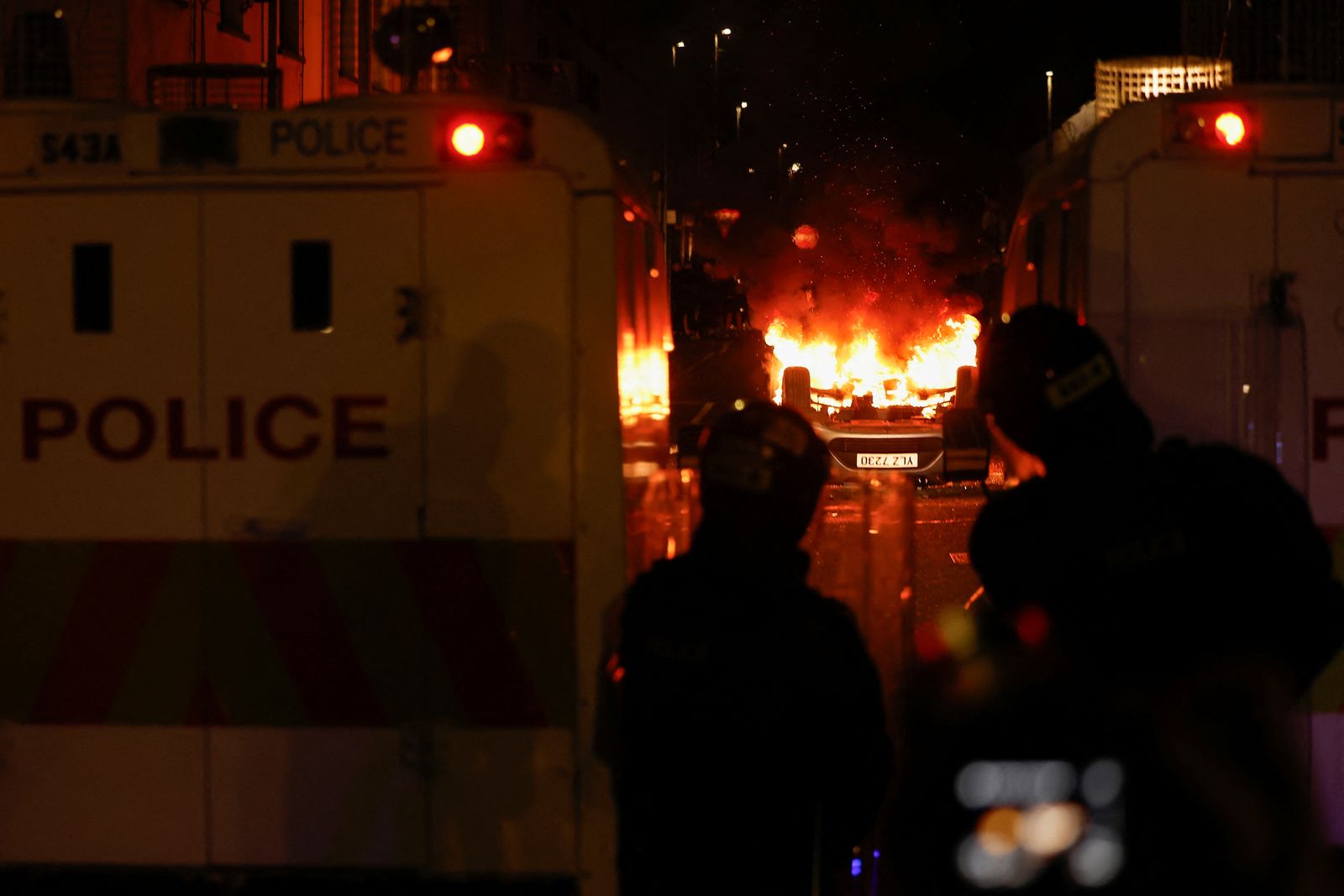 Police officers look at a burning vehicle during a second night of riots, in Ballymena, Northern Ireland, June 11, 2025. REUTERS/Clodagh Kilcoyne