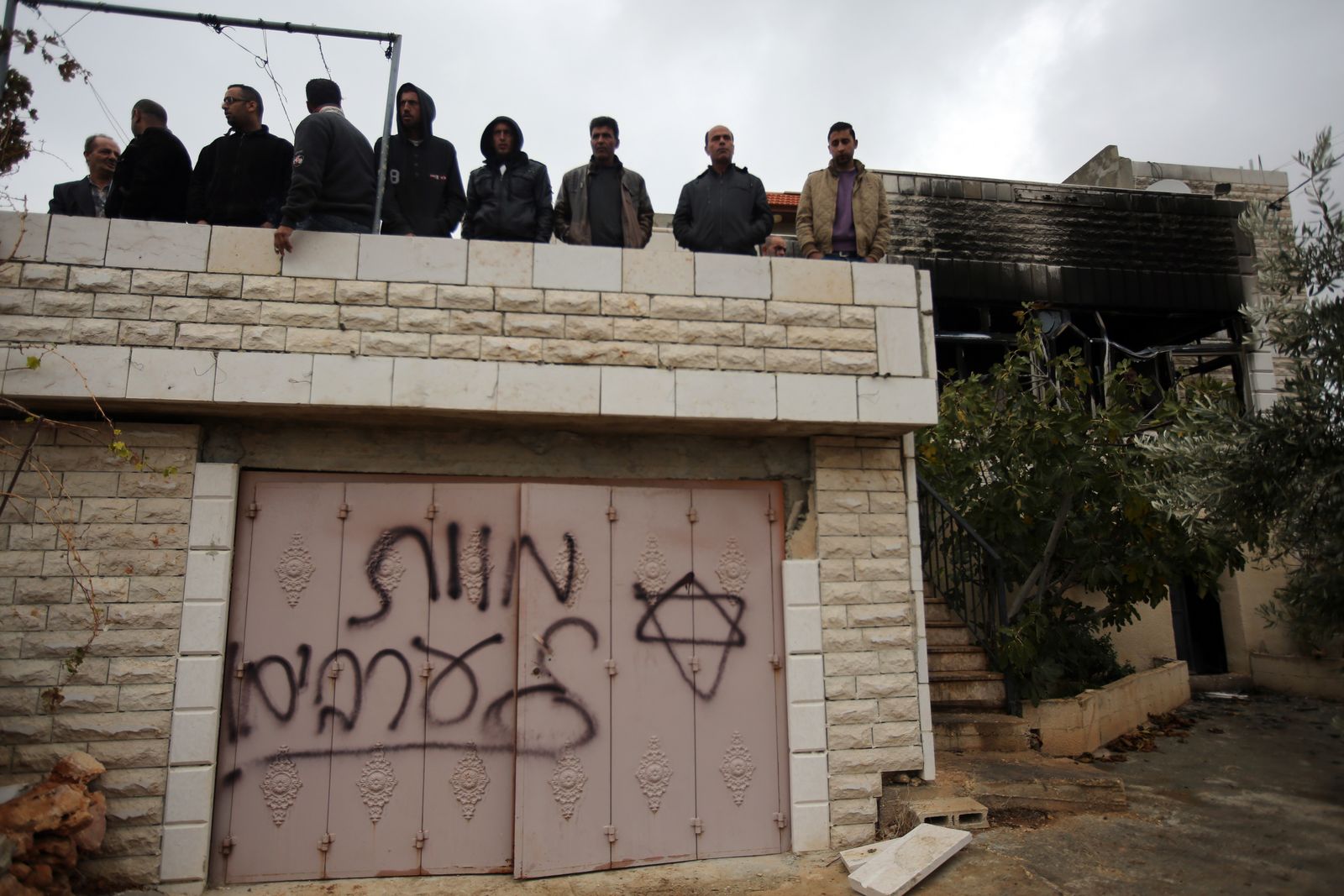 فلسطينيون بمدينة رام الله بالضفة الغربية يقفون فوق سطح مبنى  كتب عليه متطرف إسرائيلي 