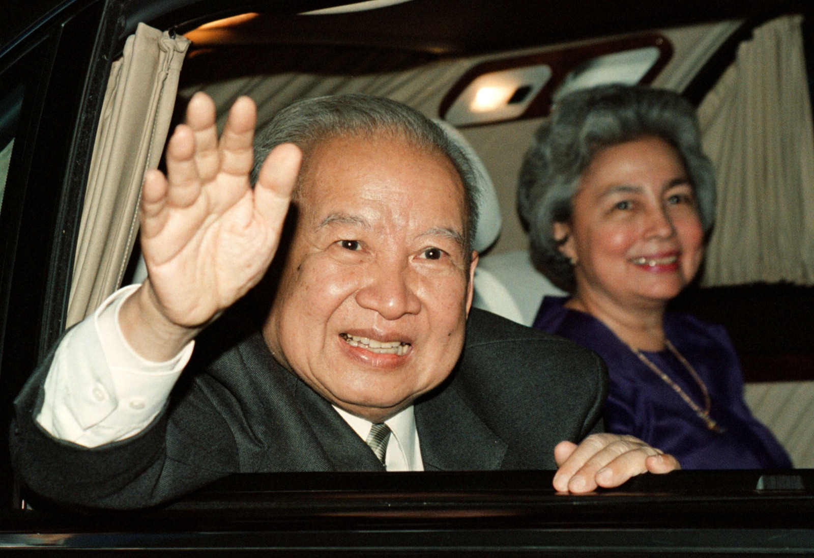 ملك كمبوديا نورودوم سيهانوك يلوح بينما تبتسم زوجته الملكة مونينيث أثناء مغادرته مطار بوتشنتونج في 23 يناير 1999